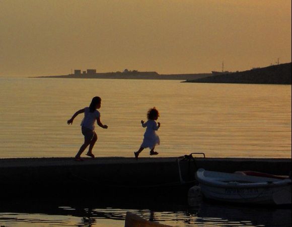 Two girls playing on a small dock at sunset. Livadia Beach, Parikia.
