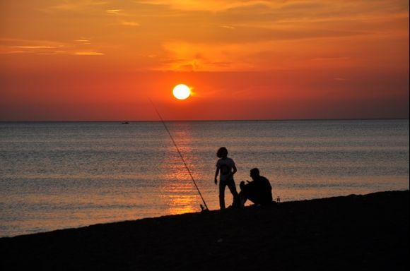 Father and daughter are fishing at the beach against sunset