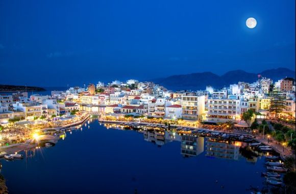 The lake Voulismeni in Agios Nikolaos at night with fullmoon, a picturesque coastal town with colorful buildings around the port in the eastern part of the island Crete.
