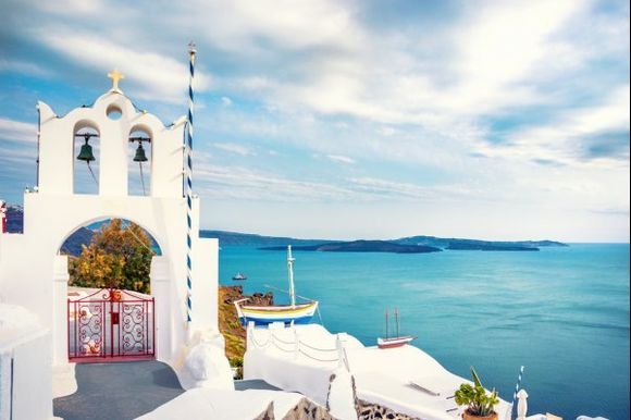 Bell tower, wooden boats and the aegean sea as seen from Oia.