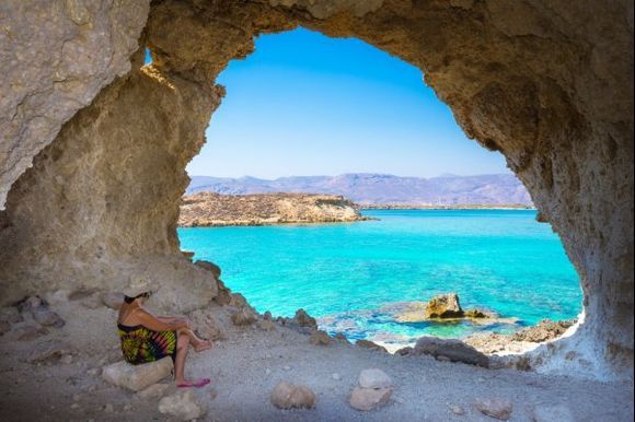 Summer view of woman in a cave at Koufonisi island in the south eastern Crete with magical turquoise waters, and ancient ruins.