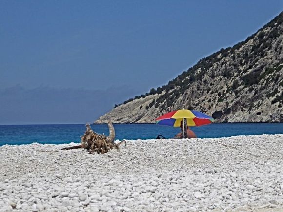 Driftwood and colourful umbrella at Myrtos beach