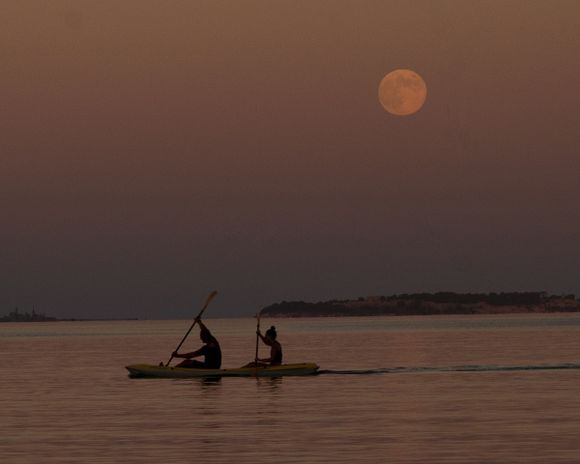 A couple kayak from Souda Beach with a full moon.