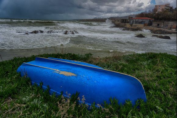 A small blue boat lies on the shore next to a rough, storm- fueled Cretan Sea.