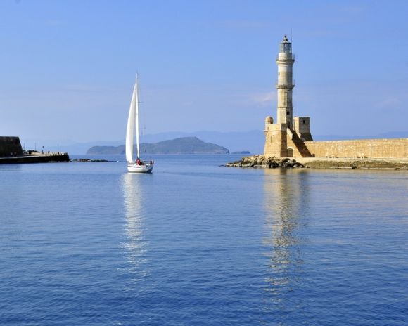A sailboat exits the Chania harbor by the Venetian lighthouse.