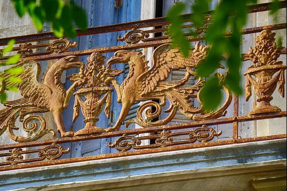 Winged Grandeur - Details of a vintage balcony railing peeking down onto a busy main street of Chania.  Years of accumulated corrosion on the striking details of the ironwork provide it with a beautiful golden color in the afternoon sunlight and hint at the possible prosperity enjoyed by residents during days gone by.