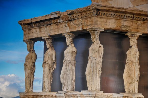 Karyatids - The Erechtheion’s best-known feature may be its south porch, whose roof, instead of being supported on columns, rested on the heads of six Korai statues – the famous Karyatids. Five of them are now in the Acropolis Museum, displayed on a special balcony and visible from all sides, while the position of the sixth Kore, still held in the British Museum, has been left empty. 
https://www.theacropolismuseum.gr/en/other-monuments-periklean-building-programme/erechtheion