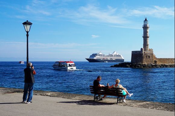 The cruise ship Azamara Pursuit sits anchored outside of Chania's Venetian harbor as its tender boats ferry passengers to and from shore.