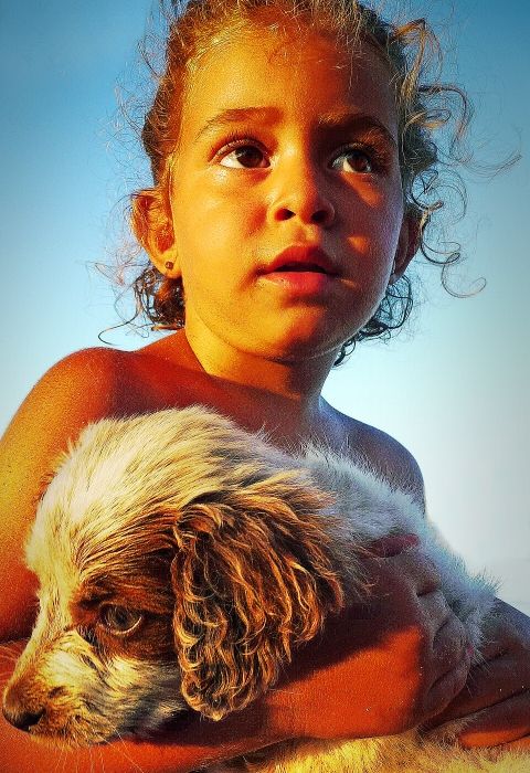 a little girl is sitting with her puppy on the beach of georgioupolis,crete