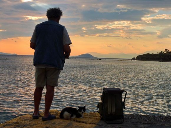 Fisherman and cat at sunset on the edge of water, Aegina town
