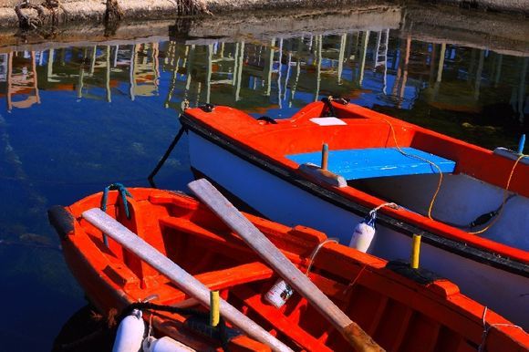 Red fishing boats and reflected taverna\'s chairs on the edge of water, Aliki