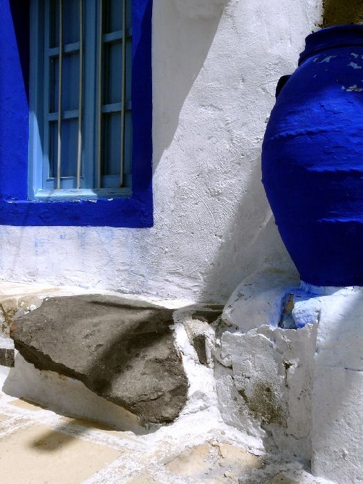 Closeup of a whitewashed house with blue window and claypot in Plaka