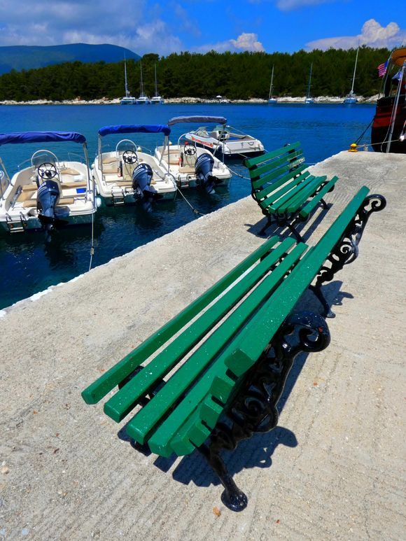 Waterfront with green benches and boats, Fiskardo