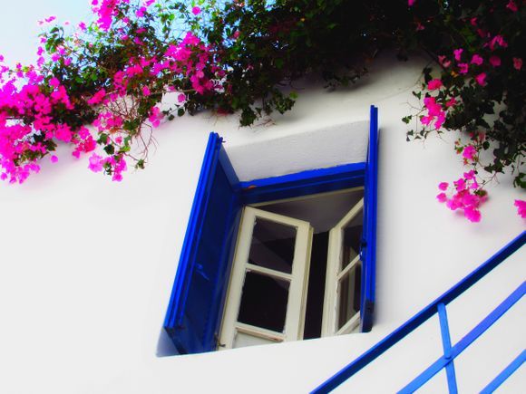 Facade with blue window framed by pink bougainvillea, Parikia