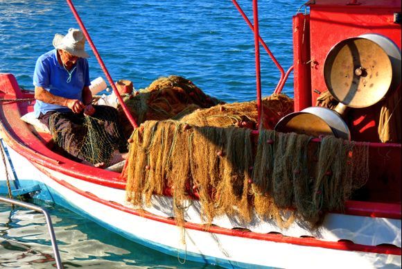 Fisherman mending fishing nets in his red boat 