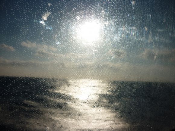 Sun on the water through water - ferry to Santorini