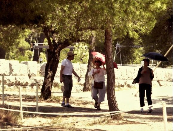 A group of tourists trying to protect themselves from the fierce sunlight wander around the ancient site of Epidaurus