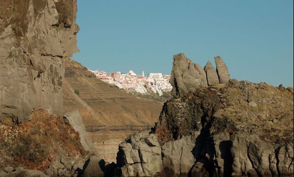 Fira in the distance shows glimpses behind the rocks.