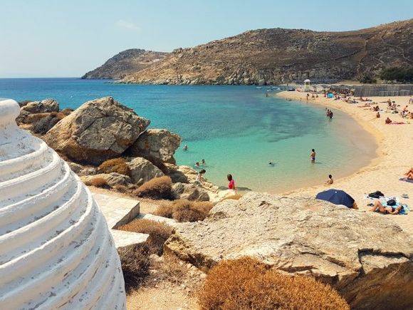 Mykonos august 2017, Agrari and Elia are located near each other, forming a huge sandy beach, 10 kilometres from the island's capital. Agrari Beach is less popular than its neighbor Elia and much calmer. They both can be reached by local bus and by taxi-boat. As with many of the beaches you approach from on high and then down a long, thin, steep road. There is a smallish cafeteria and two sets of beach loungers with shades. There are many nudists on this beach. From this beach you can walk over the rocks to the left to visit Elia beach.