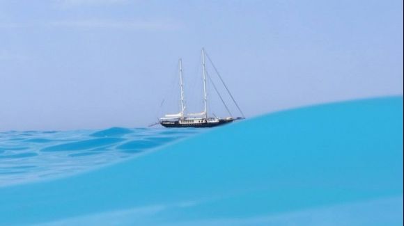Sailboat as seen from water, with turquoise sea wave caught mid-way toward me :)