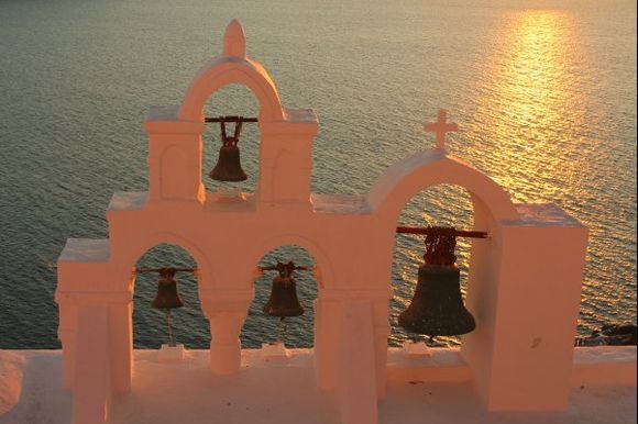 The setting sun casts a pink hue on the whitewashed bell tower - Oia village.