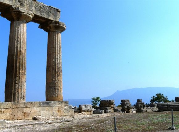 Ruins of a building/temple in Ancient Corinth. Piles of pieces of the building are waiting to be reunited with what still stands.