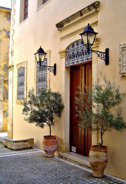 A pair of potted olive trees mark the entrance of this villa in Rethymno's old town, while ornate iron work and Victorian style lampposts add dabs of definition to the subtly stained patina.